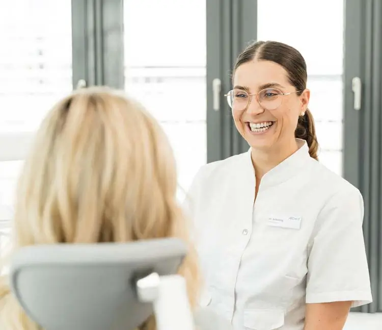 Blick &uuml;ber die Schulter der Patientin auf die l&auml;chelnde Zahn&auml;rztin