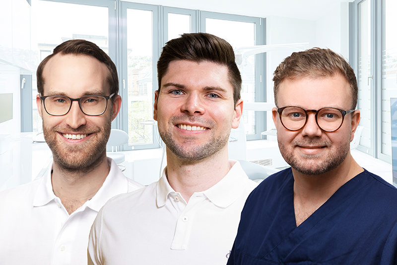 Drei Zahnärzte stehen gemeinsam in einer modernen Zahnarztpraxis und lächeln in die Kamera