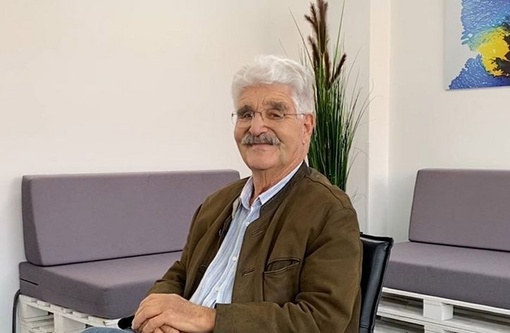 Älterer Herr sitzt in einem Wartebereich und lächelt in kamera