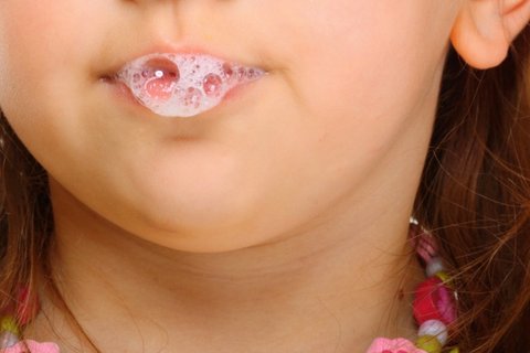 Nahaufnahme eines Kindes mit schäumendem Speichel an den Lippen. Das Kind hat braune Haare und trägt eine bunte Halskette.