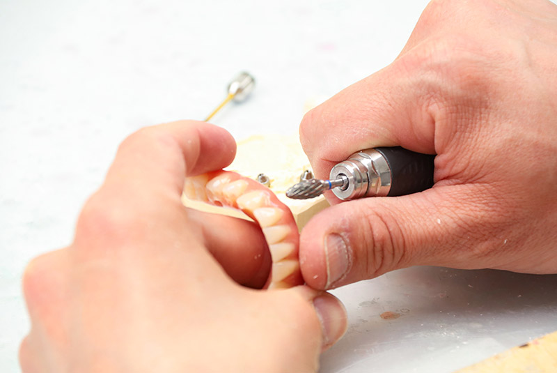 Zahntechniker hält Prothese in der linken Hand und schleift diese mit der rechten Hand
